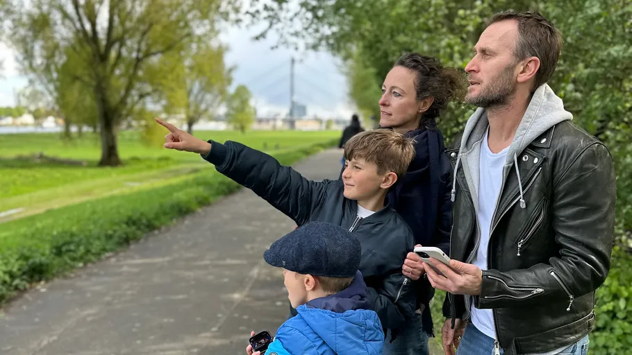 Family stands together pointing in park.