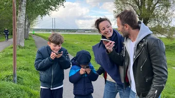 Family laughing, using phones on riverside path.