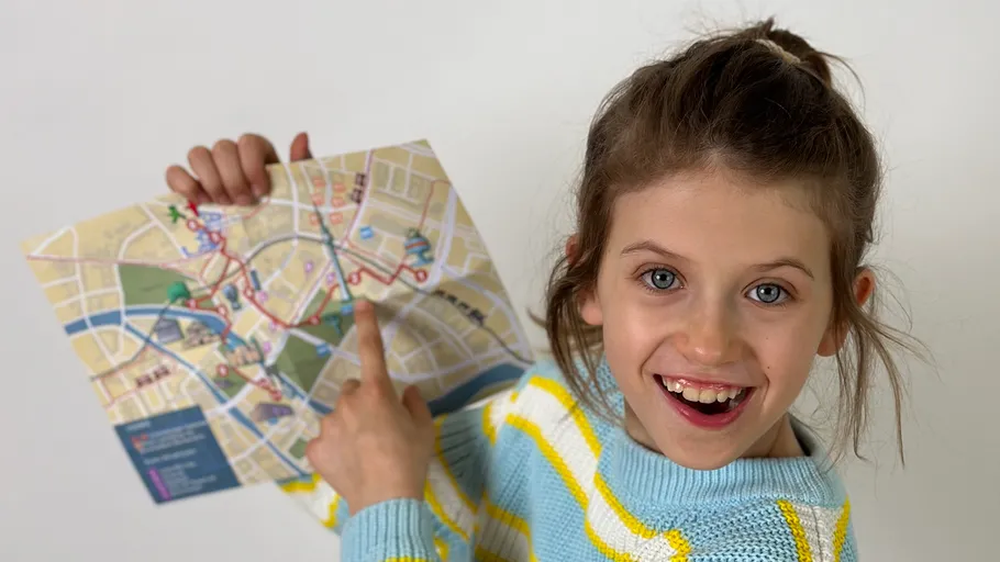 Girl pointing at map, smiling indoors.