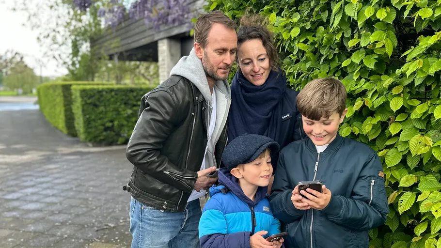 Familie draußen lächelt auf Smartphones.