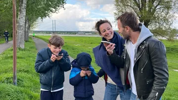 Family laughing at smartphones on a park path.
