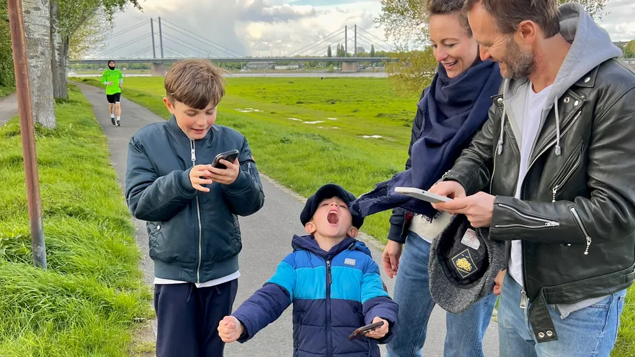 Family using phones on a riverside path.