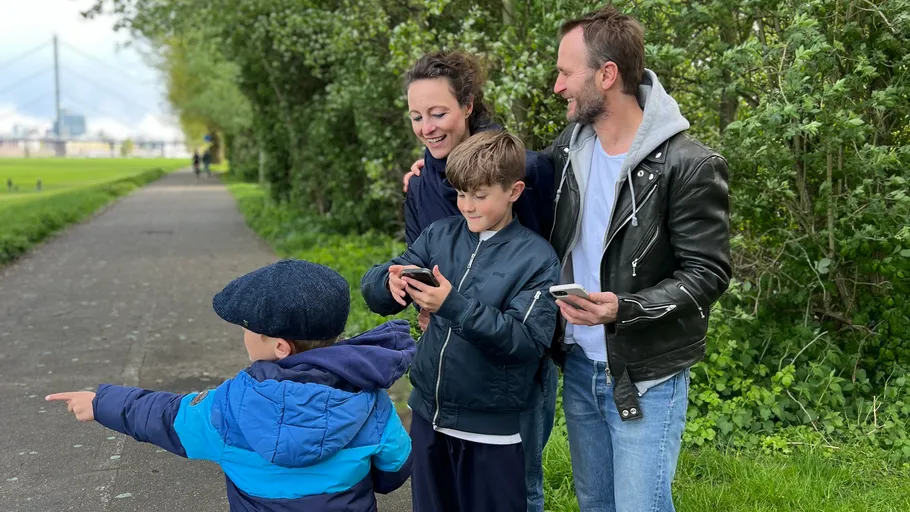 Family using smartphones on a tree-lined path.