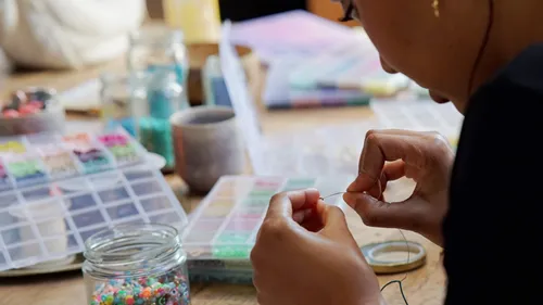 Person threading beads at a table.