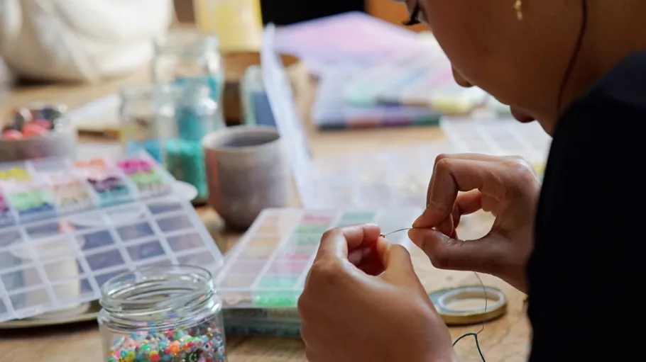 Person threading beads at a table.