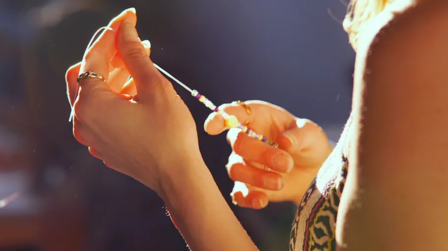 Hands threading beads in sunlight.