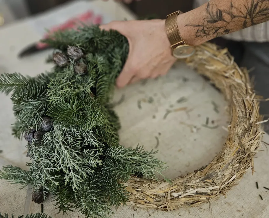 Person assembling a wreath with evergreen branches.