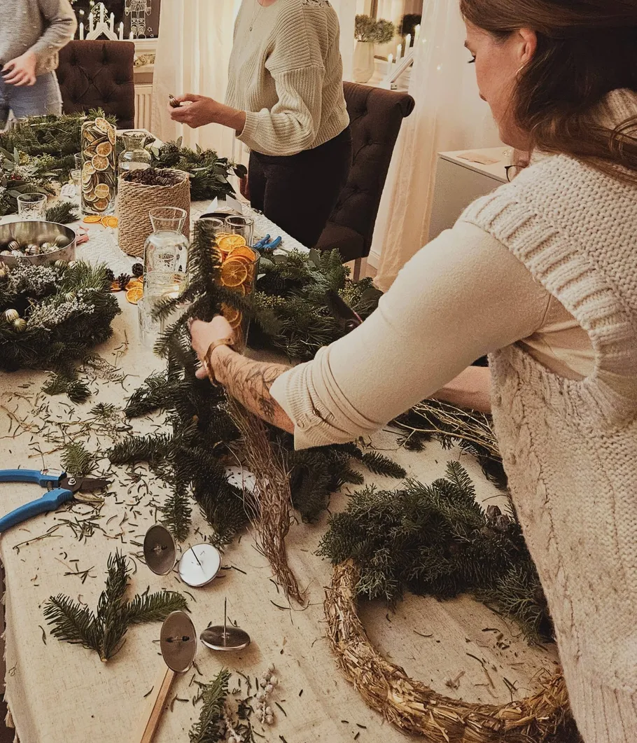 People making Christmas wreaths at a table.
