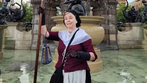Frau in historischer Tracht mit Speer, nahe Brunnen.