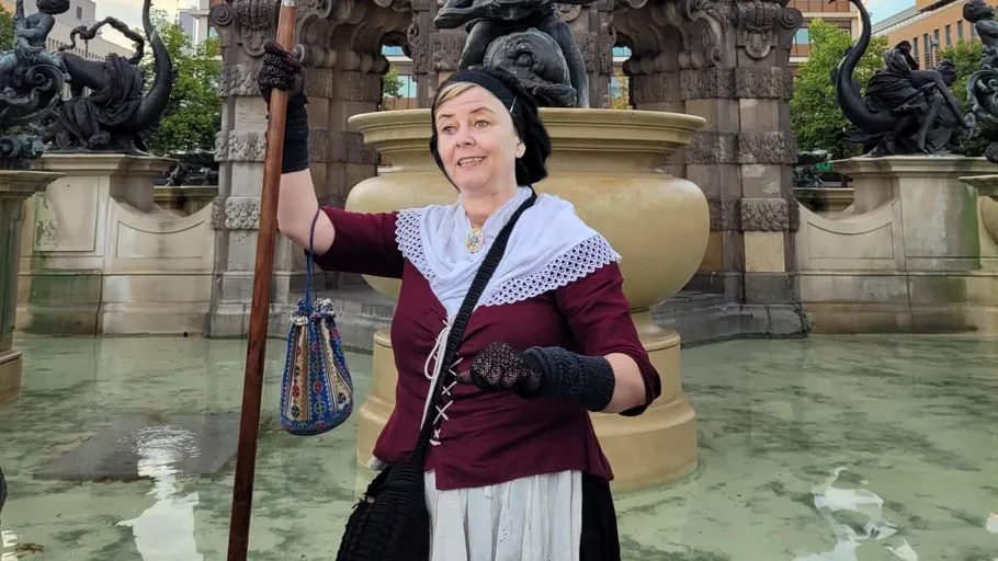 Frau in historischer Tracht mit Speer, nahe Brunnen.