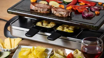 Raclette grill with meat and vegetables indoors.