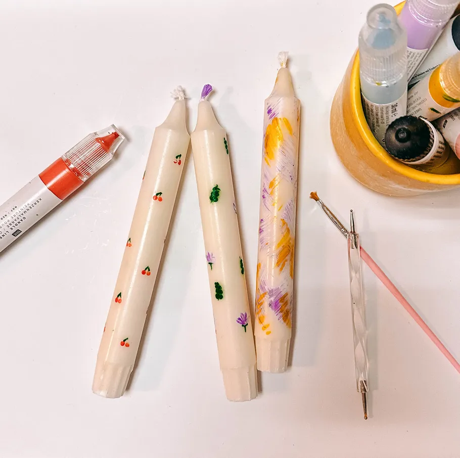 Decorated candles with painting tools on white table.