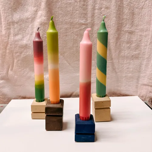 Bunte Kerzen auf geometrischen Haltern, Stoffhintergrund.