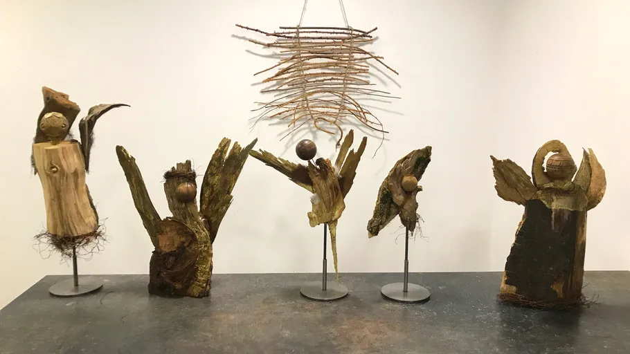 Holzskulpturen ausgestellt mit hängenden Zweigen oben.