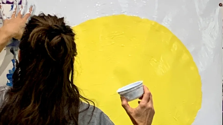 Person painting large yellow circle on canvas.