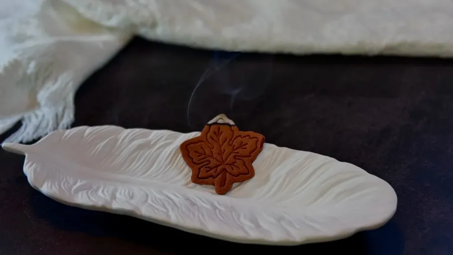 Leaf-shaped incense burning on ceramic tray.