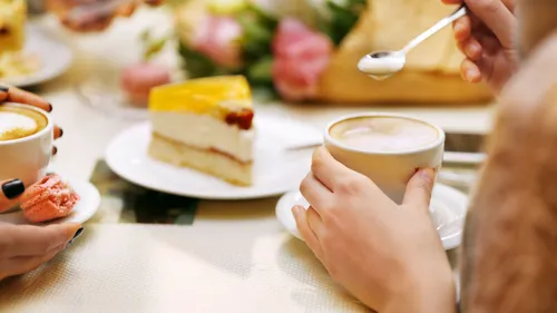 Hands holding coffee and cake on table.