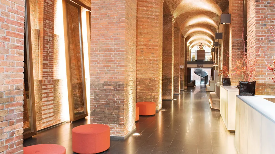 Moderner Lobbybereich mit Backsteinwänden, orange Sitzflächen.