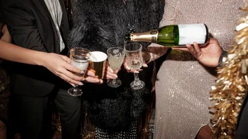 Personen gießen Champagner in Gläser bei Party.