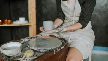 Person holding clay mug in pottery studio.