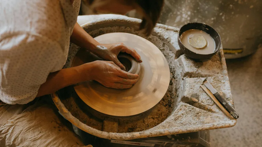Person molding clay on pottery wheel indoors.