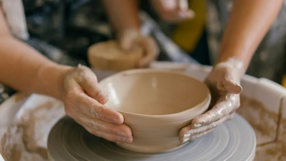 Hands shaping clay bowl on pottery wheel.