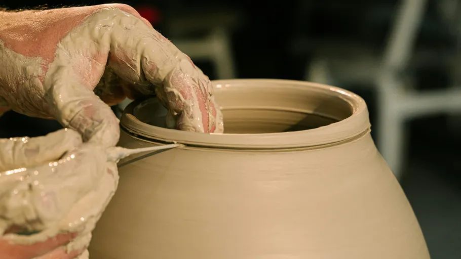 Hands shaping clay pot with tools.