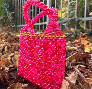 Pink beaded handbag on autumn leaves outdoors.
