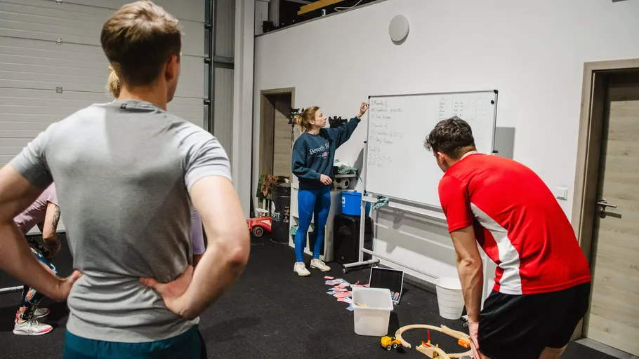 Group listens to woman explaining on whiteboard indoors.