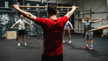 Menschen trainieren mit Holzstöcken im Fitnessstudio.