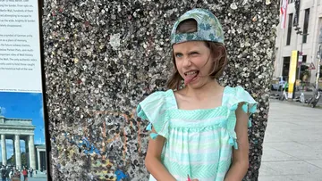 Child making a funny face beside mosaic wall.