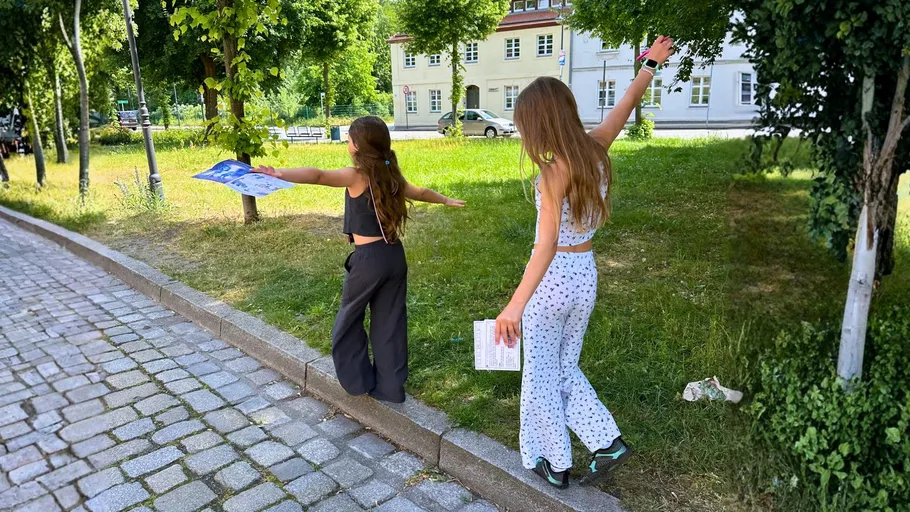 Two girls balancing on a curb in a park.