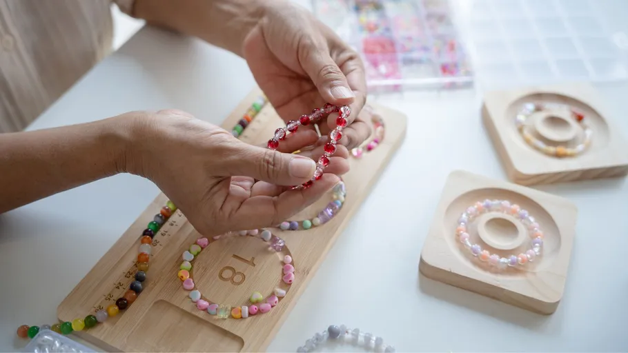Hands making beaded bracelets on wooden board.