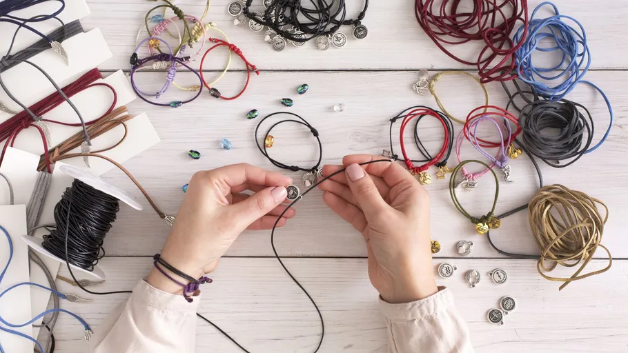Hands crafting bracelets on wooden table.
