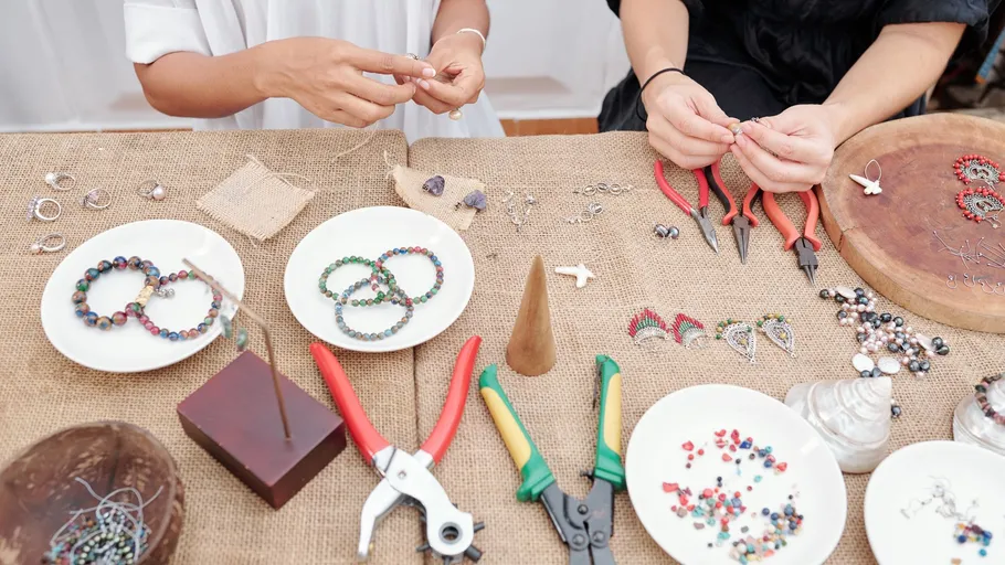 Hands crafting jewelry on burlap-covered table.