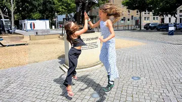 Two children high-five near a statue outdoors.