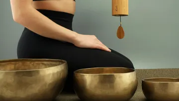 Person kniet neben tibetischen Klangschalen, meditative Umgebung.