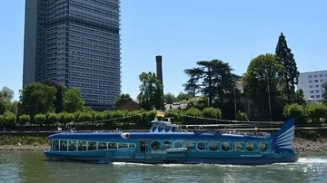 Blue boat sailing past tall building, trees.