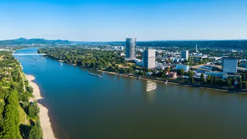 Fluss mit Stadtsilhouette und grünen Hügeln.