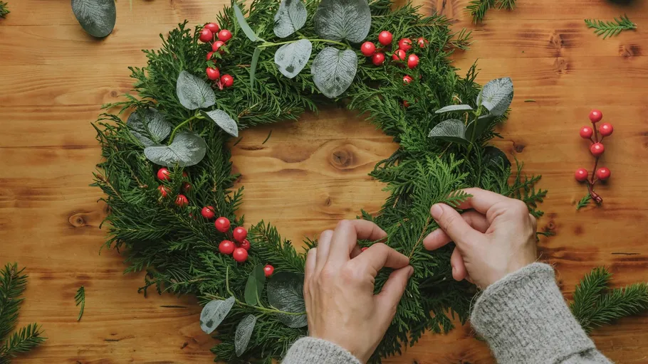 Hands decorate a wreath on wooden table.