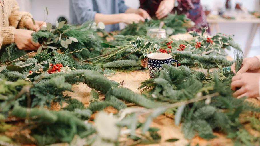 People crafting holiday wreaths on a table.