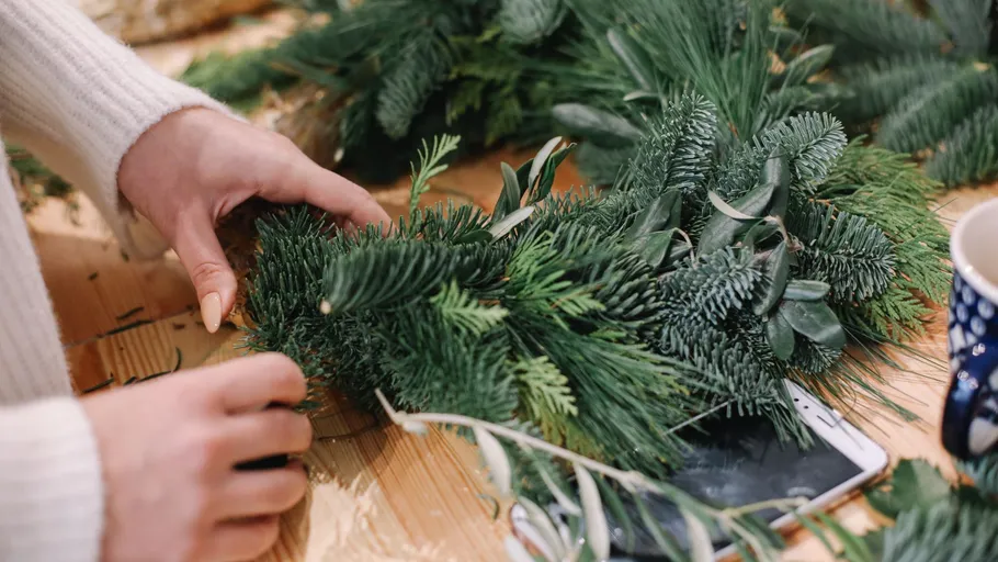 Person crafting a wreath on a table.