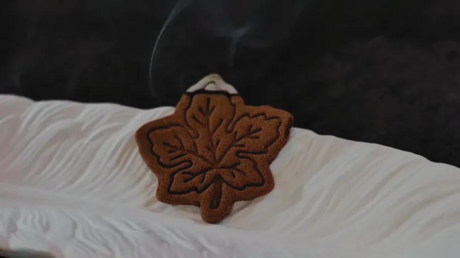 Maple leaf incense burning on white tray.