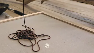 Brown cord spiraling onto mesh surface, wooden background.