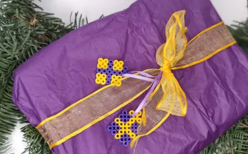Lila Geschenk mit gelbem Band, grüne Zweige.
