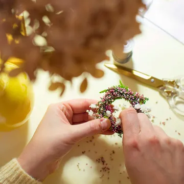 Hands crafting floral wreath on a table.