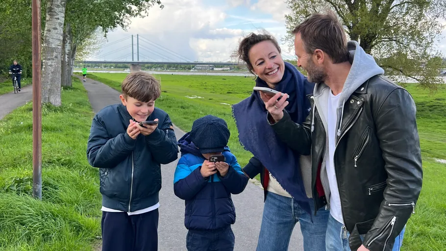 Family laughing with phones near riverbank.