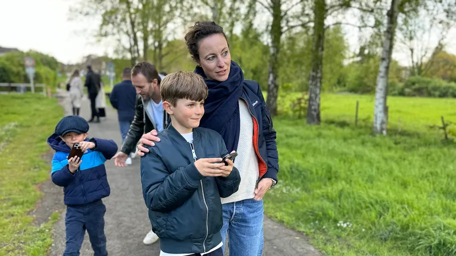 Family on pathway using phones; trees around.