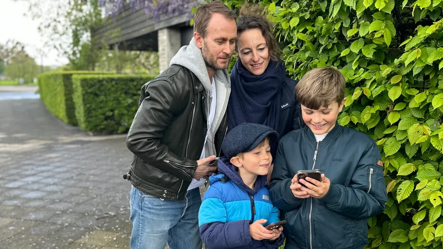 Family looking at phones near green bushes.