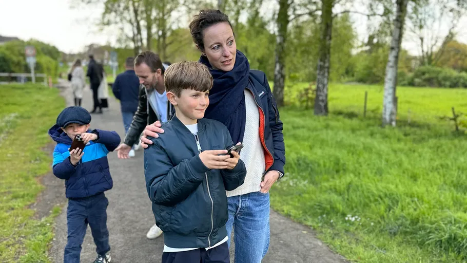 Family walking on path, holding devices, green scenery.